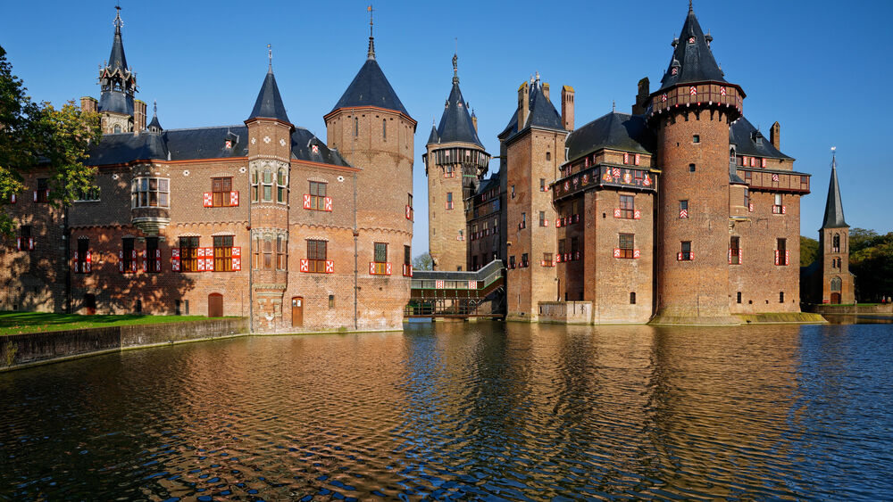 Обои для рабочего стола Замок Дер Хаат / De Haar Castle, Нидерланды / Netherlands, из красного кирпича с многочисленными башнями и остроконечными крышами стоит на воде, на фоне голубого неба