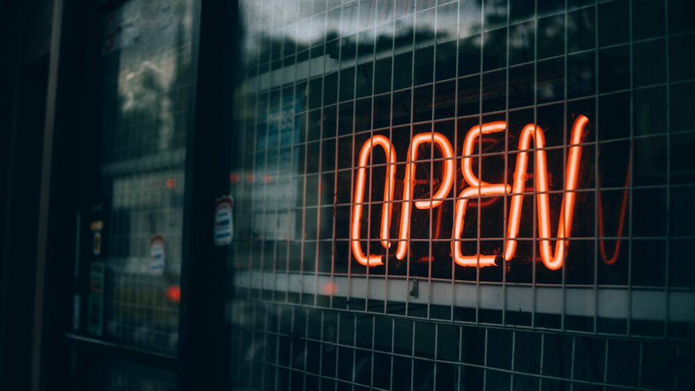 Обои для рабочего стола Красная неоновая вывеска с надписью OPEN за металлической решеткой и стеклом на фоне размытого отражения