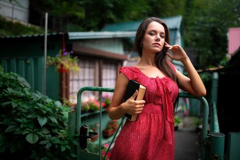 Обои на рабочий стол Модель Катя в красном платье в горошек и с книгой в руке стоит у калитки загородного дома