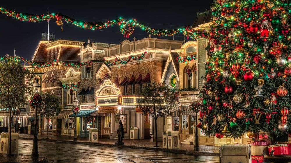Обои для рабочего стола Диснейленд / Disneyland, США / USA, большая украшенная новогодняя елка на пустой улице на фоне зданий, декорированных гирляндами и праздничными огнями