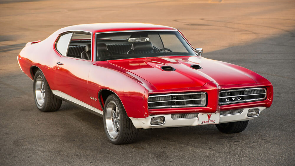 Обои для рабочего стола Двухдверный автомобиль Pontiac GTO красного цвета стоит на асфальтированной дороге