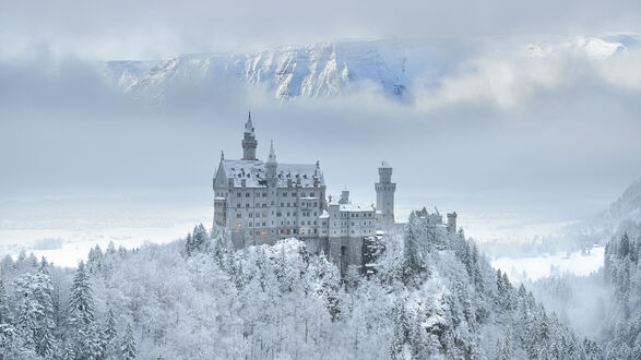 Обои на рабочий стол Замок Нойшванштайн / Neuschwanstein Castle, Германия / Germany, на заснеженном холме среди деревьев, на фоне заснеженных гор и облаков