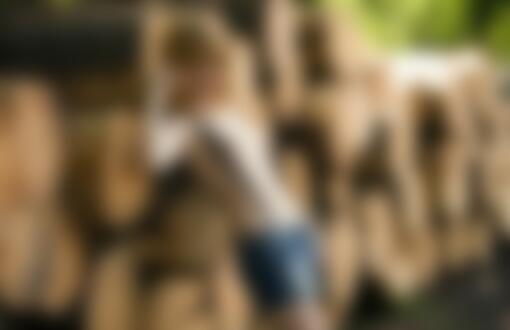 Обои на рабочий стол Девушка в джинсовых шортах с черными подтяжками с обнаженной грудью оперлась спиной о большие бревна