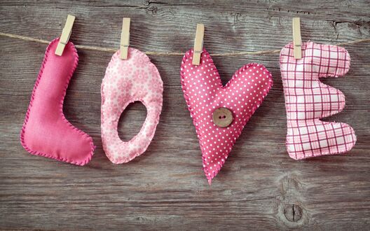 Обои на рабочий стол Четыре розовые тканевые буквы, образующие слово LOVE, висят на веревке с прищепками на фоне деревянной поверхности