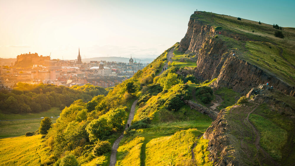 Обои для рабочего стола Эдинбург / Edinburgh, Шотландия / Scotland, зеленый холм с тропами и людьми, на фоне городского пейзажа с замком