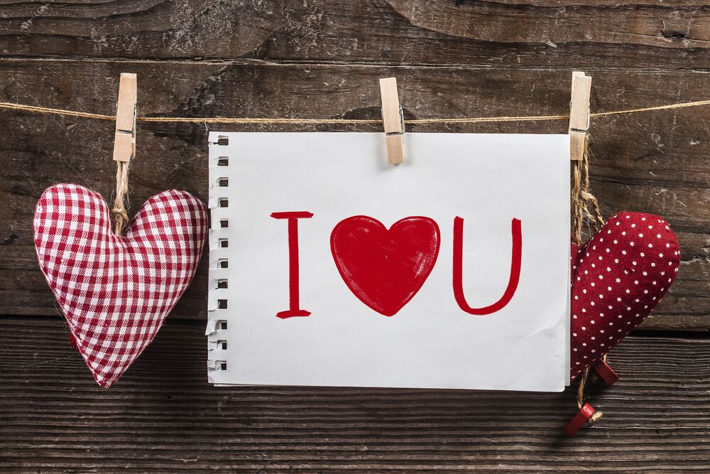 Обои для рабочего стола Белый лист бумаги с надписью (I ❤️ U) и два тканевых сердца, атрибуты Дня святого Валентина / Valentines Day, висят на веревке на фоне деревянной стены