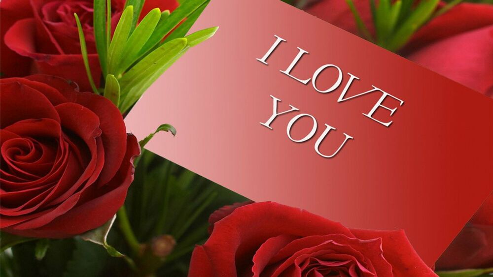Обои для рабочего стола Красная карточка с надписью (I LOVE YOU) на букете красных роз и зеленых листьев на размытом красном фоне