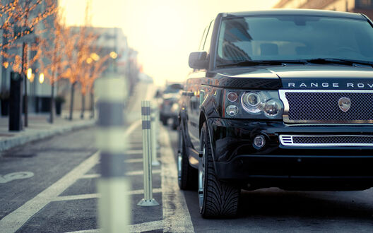 Обои на рабочий стол Черный внедорожник Range Rover припаркован на обочине городской улицы, на фоне зданий и деревьев с огнями
