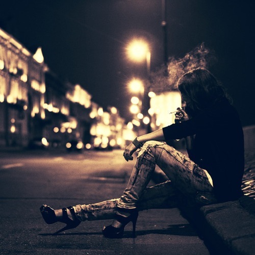 Фото Грустная девушка курит, присев на обочине дороги ночного города