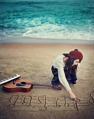 Фото Девушка рисует пальцем на морском песке ноты