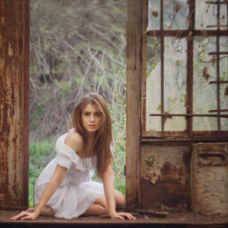Фото Красивая девушка в белом платьице сидит в дверном проёме заброшенного дома