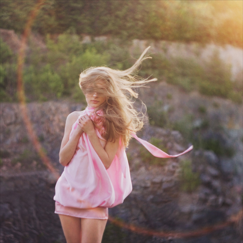 Фото Красивая девушка в розовом платьице с развевающимися на ветру волосами в лучах солнца на природе