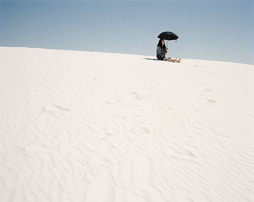 Фото Девушка сидящая с черным зонтом на песке