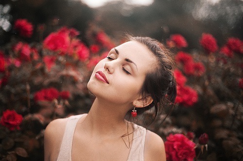Фото Мечтательная девушка с закрытыми глазами стоит среди красных роз