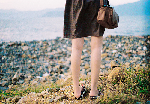 Фото Девушка с сумкой в коричневом ситцевом платье смотрит на море