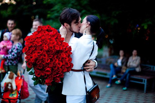 Фото Мужчина с девушкой целуются на улице держа большой букет роз в руках