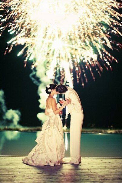 Фото Жених и невеста с бокалами в руках целуются на фоне фейерверка