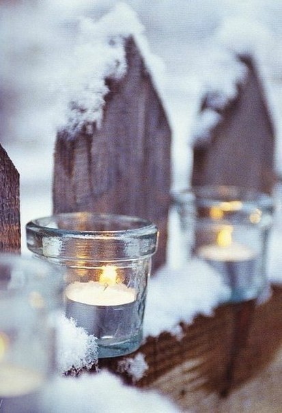 Фото Свечи в прозрачных стаканчиках стоят на покрытом снегом заборе