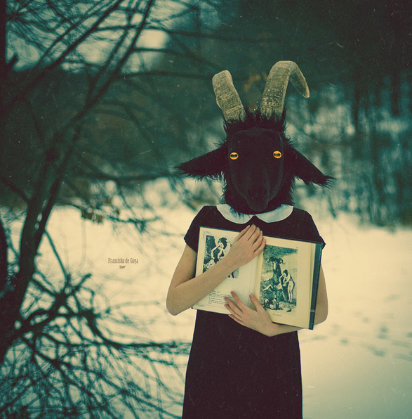 Фото Девушка с головой черной козы стоит в зимнем лесу с раскрытой книгой