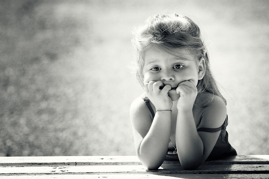 Фото Маленькая девочка оперлась на локотки, поднесла пальчики ко рту и грустит