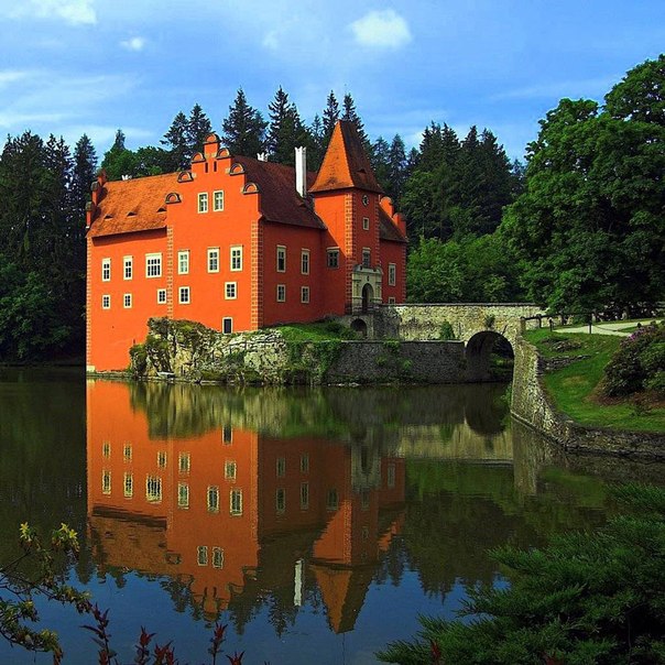 Фото Красивый старинный замок, стоящий на берегу озера с каменным мостиком, ведущим к парадному входу, в окружении густой зелени