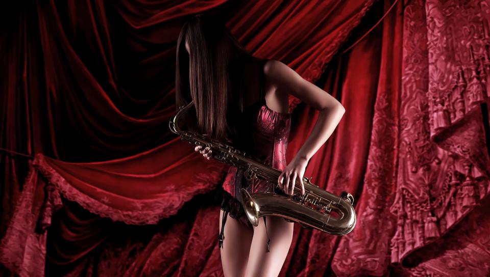 Фото Длинноволосая девушка-шатенка увлеченно играет на саксофоне на фоне красной портьеры