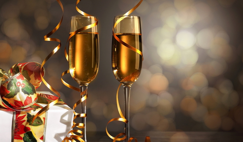 Два бокала с шампанским, обвитые ленточками серпантина, рядом новогодние подарки
