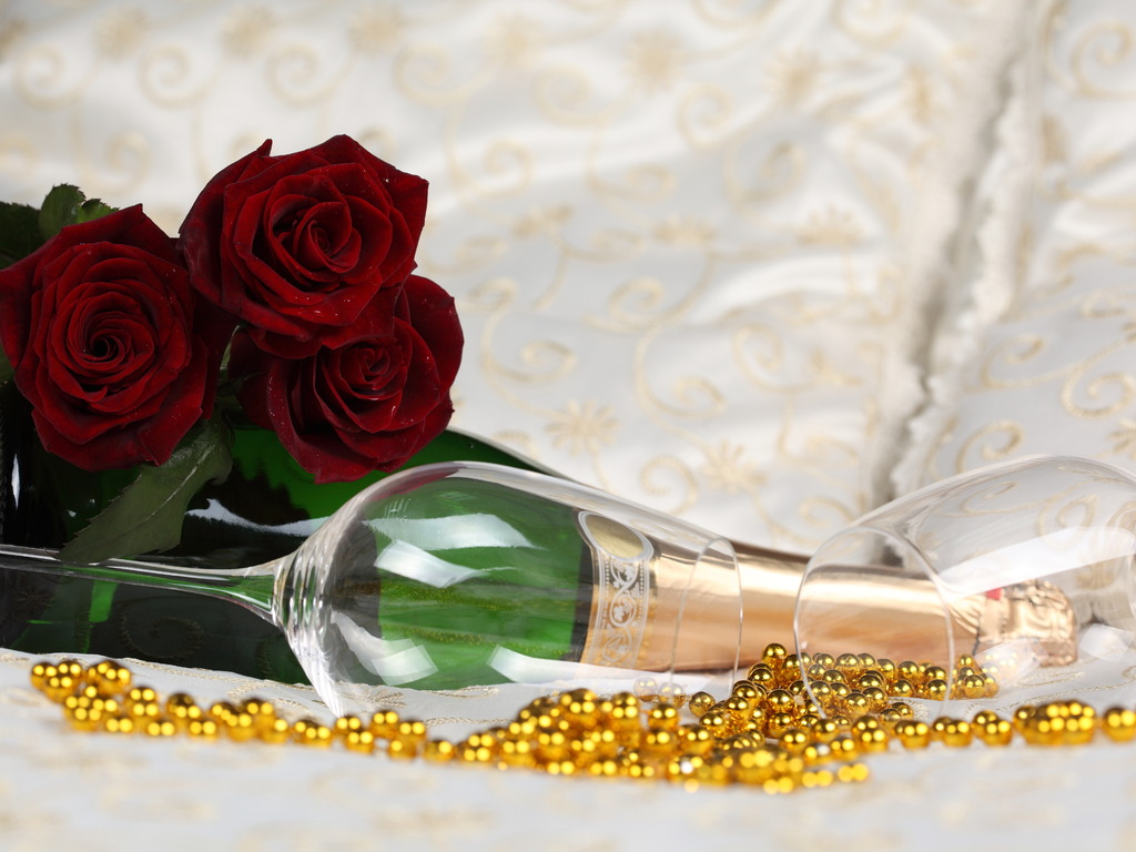 Фото Букет бордовых роз, бутылка шампанского, фужер и россыпь бусинок на белой драпировке