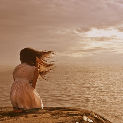 Фото Девушка с развевающимися волосами сидит на коленях перед морем