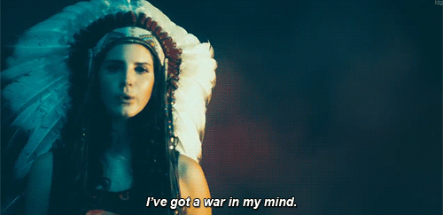 Фото Американская певица Лана Дель Рей / Lana Del Rey в Солнечном головном уборе индейцев подносит пистолет в голове (I've got a war in my mind / Война в моей голове)