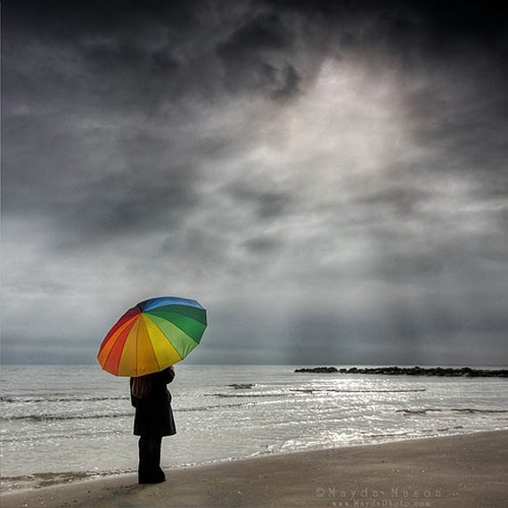 Фото Девушка стоит с радужным зонтом в пасмурную погоду на берегу моря