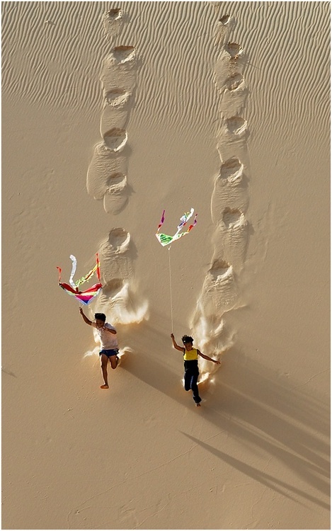 Фото Дети с воздушными змеями бегут по песку, оставляя следы