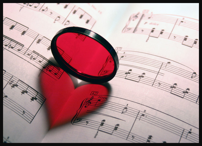 Фото Красное стеклышко стоит на ребре создавая иллюзию сердечка на сгибе нотной тетради