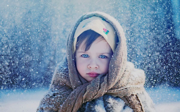 Фото Девочка с синими глазами, в двух платках и шубке, стоит под снегопадом