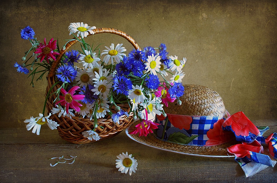 Фото На столе стоит плетеная корзинка с цветами, и лежит соломенная шляпка с цветным бантом