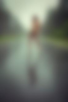 Фото Полуобнаженная девушка прикрыв рукой грудь стоит по среди дороги под дождем
