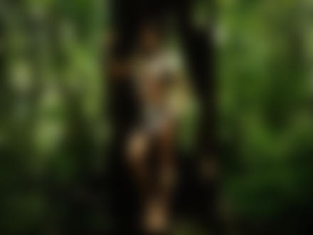 Фото Полуобнаженная девушка в наряде индейца стоит в лесу у дерева