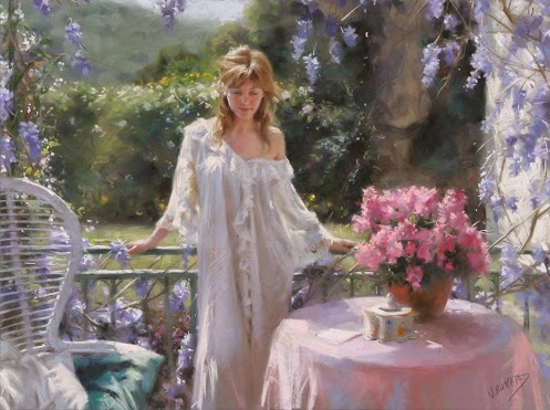 Фото Девушка в белом платье положив руки на зеленую ограду стоит рядом у стола с розовой скатертью и вазой розовых цветов