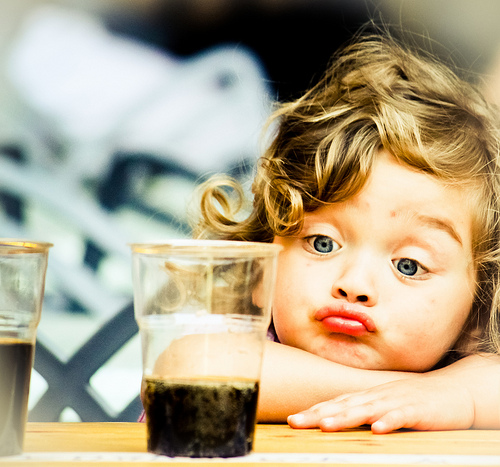 Фото Девочка пучит губки смотря на напиток в стакане