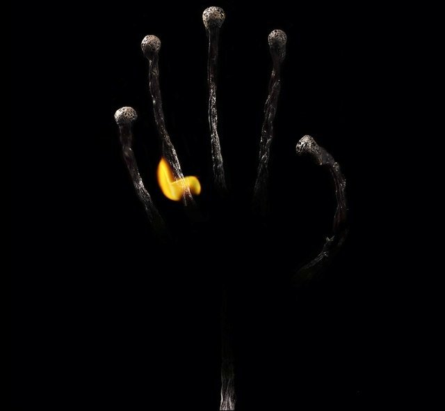 Фото Кисть руки из сгоревших спичек на черном фоне и огонь