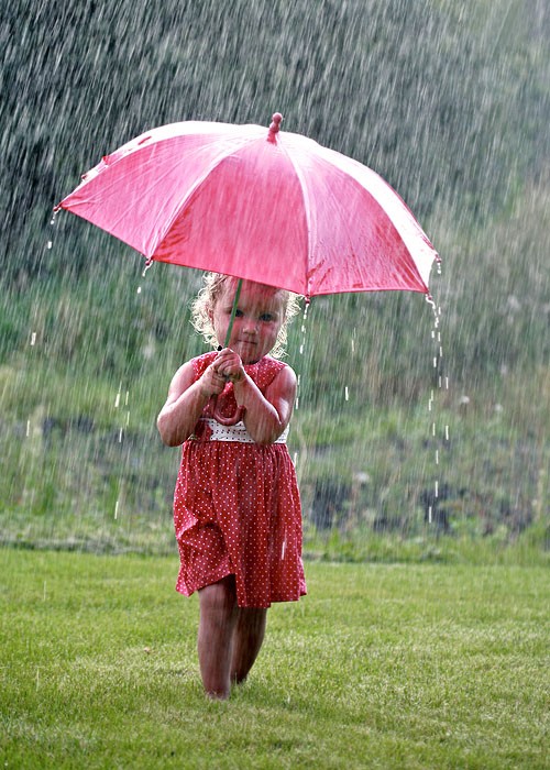 Фото Девочка стоит под розовым зонтом в дождь в красном платье в белый горошек