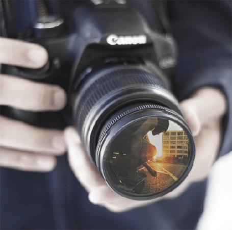 Фото Мужчина держит в руках фотоаппарат фирмы Canon, в котором видно, как другой мужчина прыгает на скейтборде
