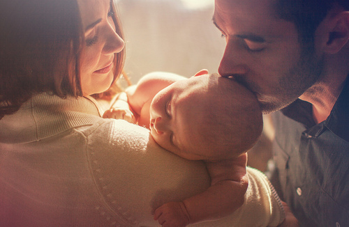 Фото Девушка держит малыша на руках, а мужчина целует его в головку