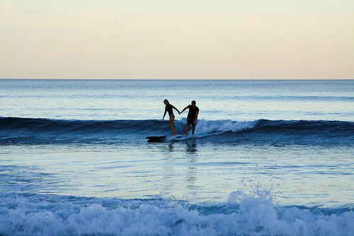 Фото Девушка с мужчиной держатся за руки катаясь по волнам на доске