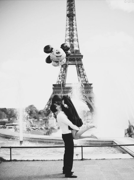 Фото Мужчина поднял девушку, в руках которой находятся воздушные шары, на фоне Эйфелевой башни