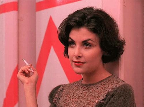 Фото Актриса Sherilyn Fenn / Шерилин Фенн стоит у стены с сигаретой в руках и улыбается, кадр из сериала Twin Peaks / Твин Пикс