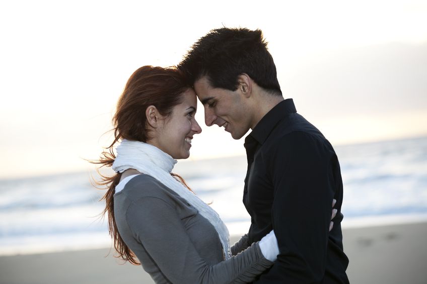 Фото Девушка с парнем улыбаются друг другу, уткнувшись лбами на фоне моря и неба
