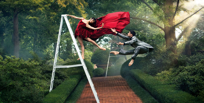 Фото Девушка в красном платье стоит на лестнице и красиво склоняется к мужчине в деловом костюме, который подает ей руду в прыжке, фотограф Cade Martin / Кейд Мартин