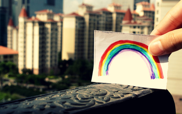 Фото Девушка держит рисунок радуги на бумаге и держит его над городом