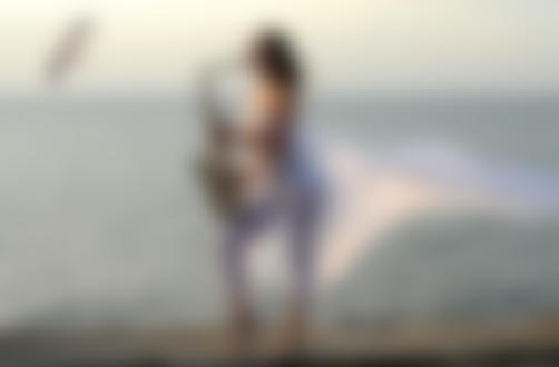Фото Обнаженная девушка в прозрачном парео играет на саксофоне на берегу моря